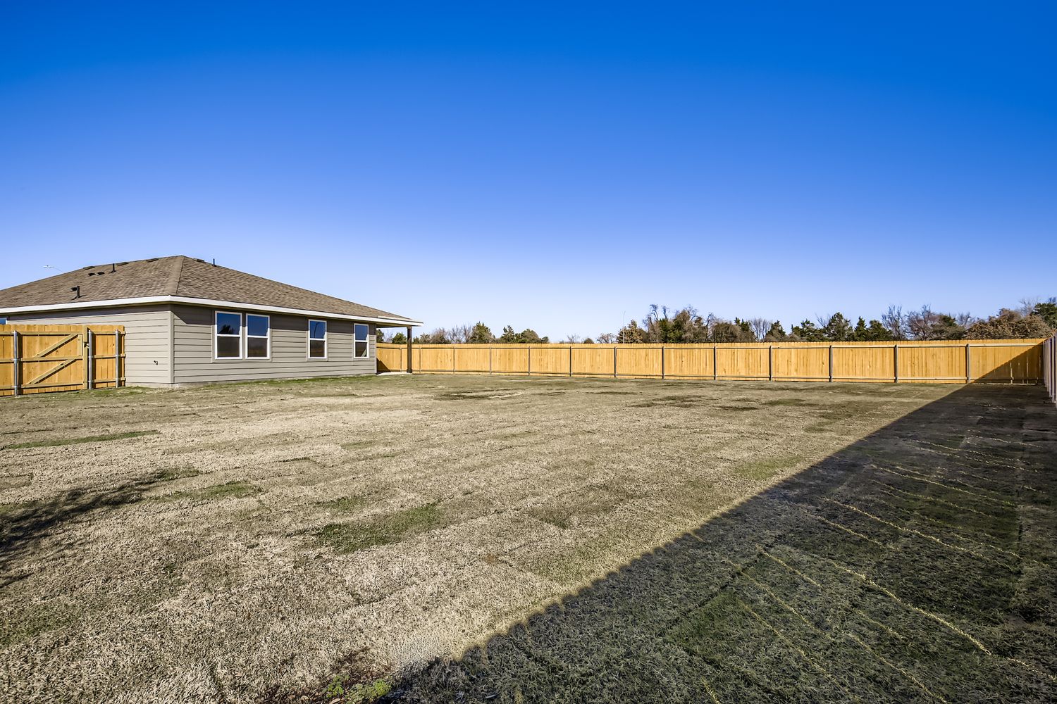 A large field with a fence and a house in the background.