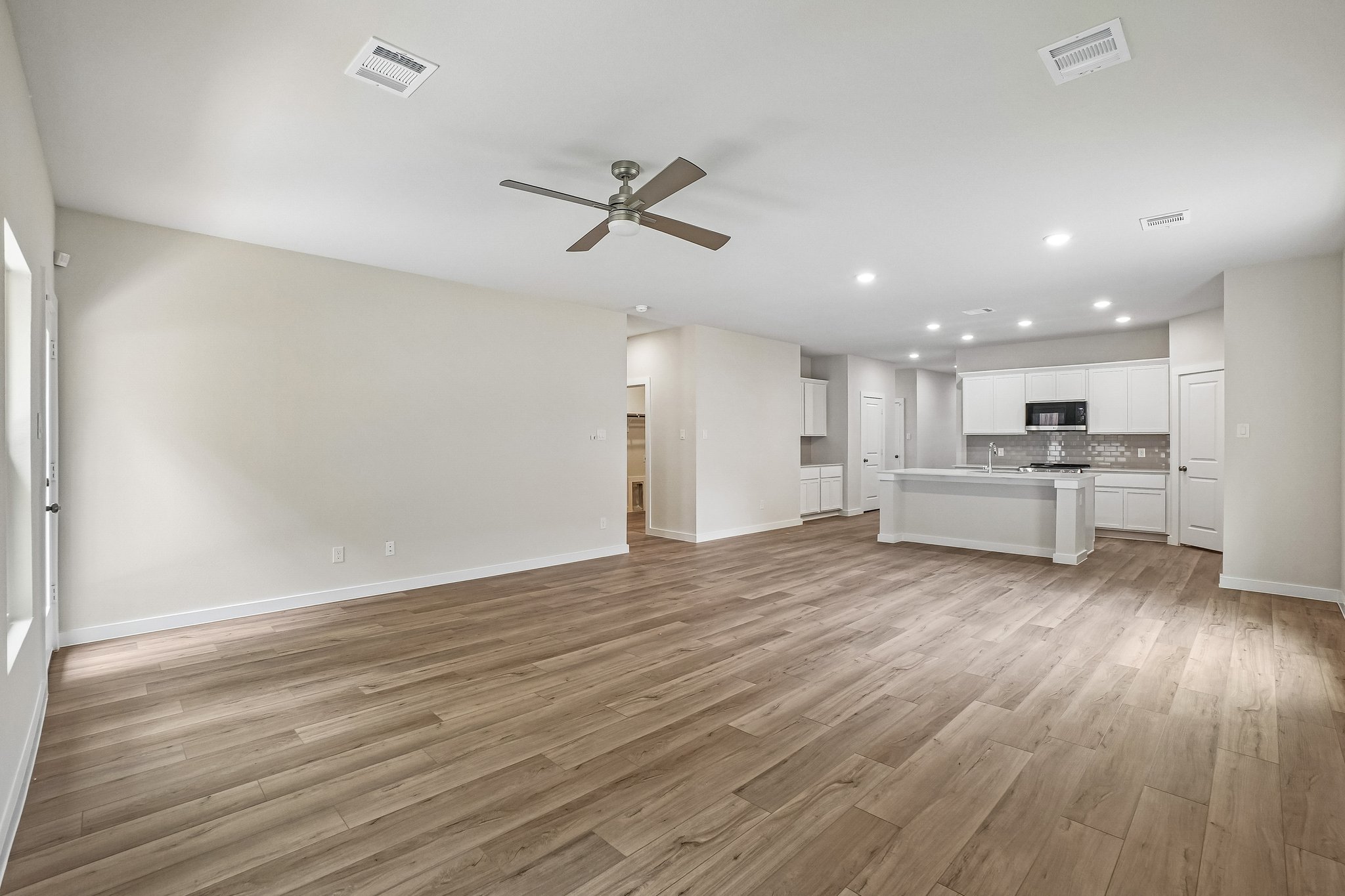A large empty room with a wood floor and a ceiling fan.