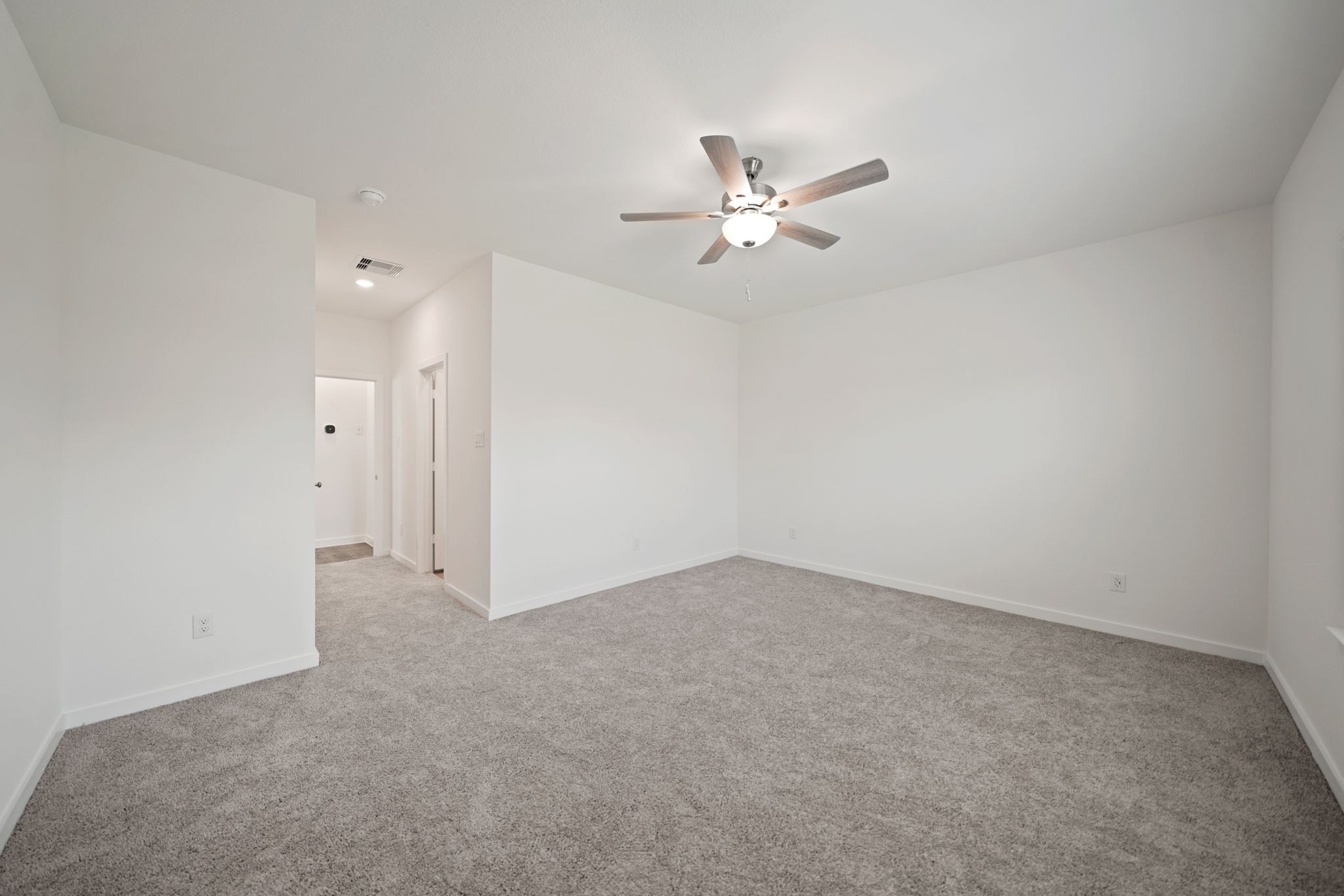 A room with a ceiling fan and a carpet.