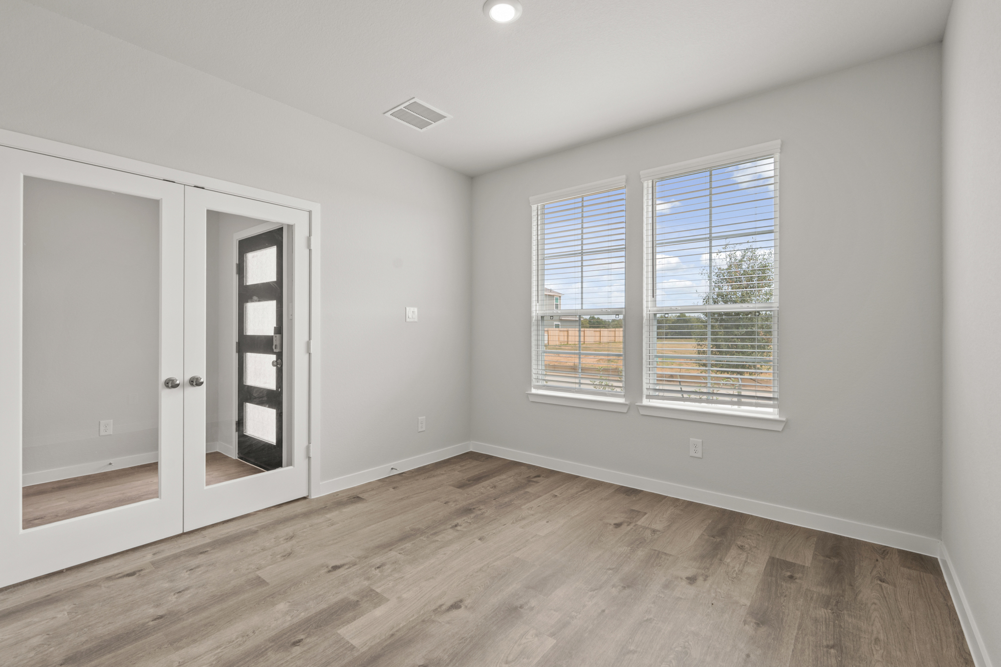 A room with a wood floor and a window with blinds.